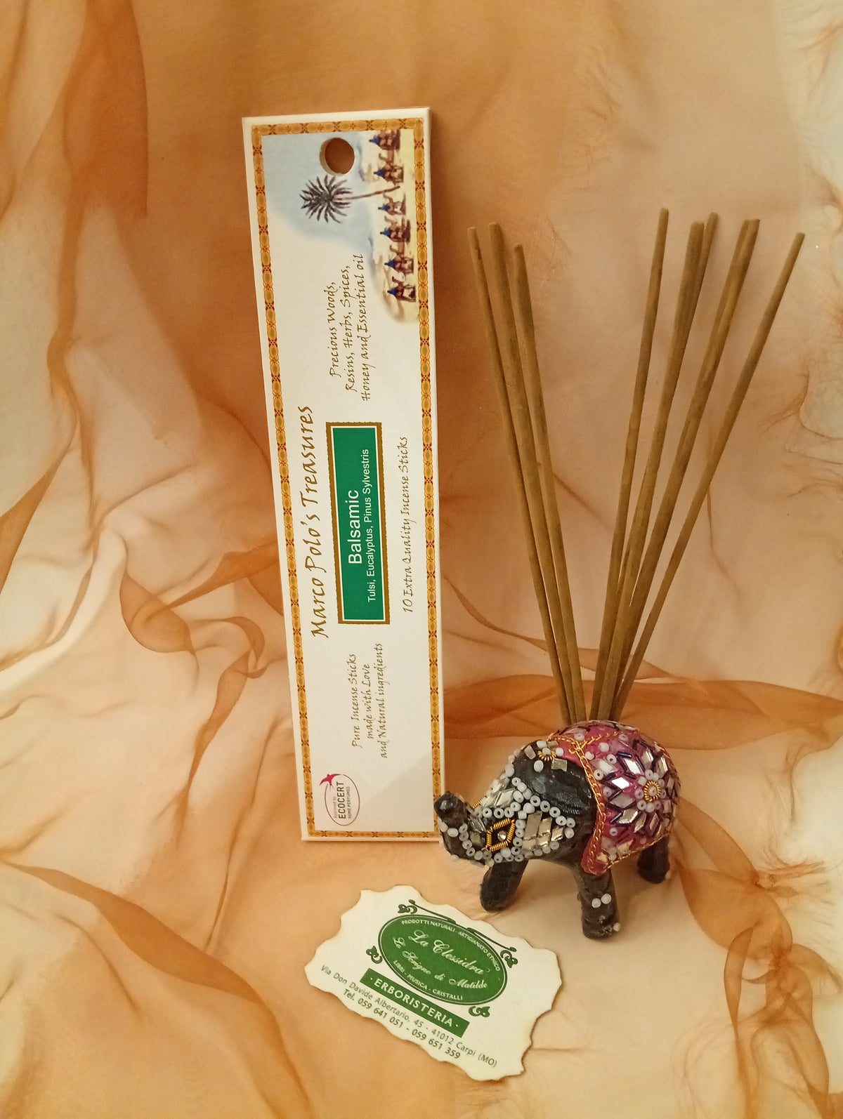 Incenso Balsamic Fiore d'Oriente Linea Marco Polo's Treasures con astuccio ben visibile, mazzetto di incensi dritti, biglietto da visita e velo sullo sfondo, esposto in negozio da Erboristeria La Clessidra Carpi.