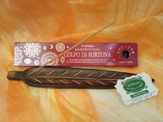 Confezione orizzontale di Incenso Goloka Manifestation Colpo di Fortuna con Giada Verde burattata, davanti a un portaincenso artigianale a forma di foglia con stick, biglietto da visita dell’Erboristeria La Clessidra Carpi e sfondo con telo sfumato in toni aranciati orientali.