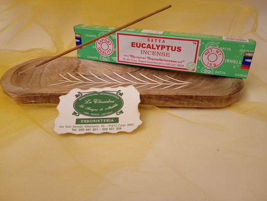 Confezione di Incenso Eucalyptus (Eucalipto) Satya appoggiata trasversalmente su portaincenso di legno con biglietto da visita dell’Erboristeria La Clessidra Carpi e sfondo in velo di organza gialla