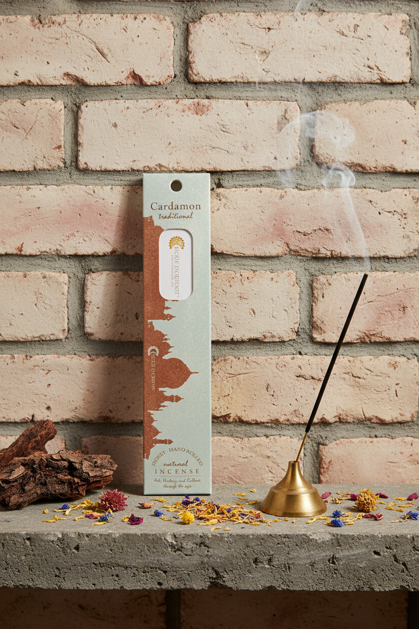 Incenso Cardamon Cardamomo Fiore d'Oriente Linea Traditional con stick acceso in portaincenso di ottone, cortecce e fiori su base di pietra e muro antico, da Erboristeria La Clessidra Carpi