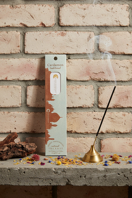 Incenso Cardamon Cardamomo Fiore d'Oriente Linea Traditional con stick acceso in portaincenso di ottone, cortecce e fiori su base di pietra e muro antico, da Erboristeria La Clessidra Carpi