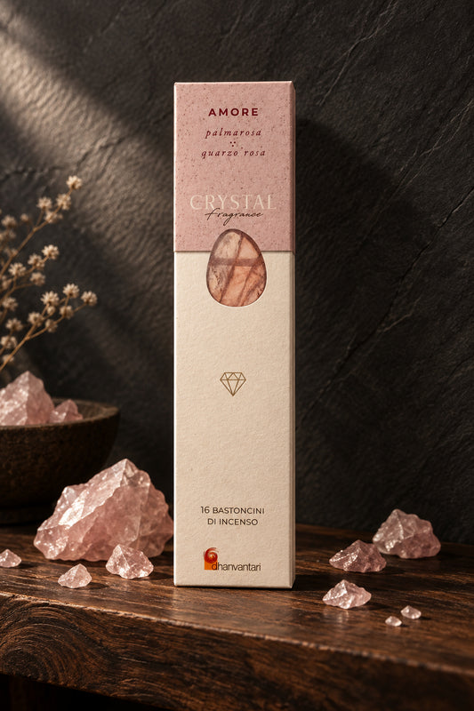 Astuccio rettangolare verticale di Incenso Crystal Fragrance Amore Dhanvantari su mensola di legno scuro davanti a una parete di ardesia con frammenti grezzi di pietra quarzo rosa, da Erboristeria La Clessidra Carpi.