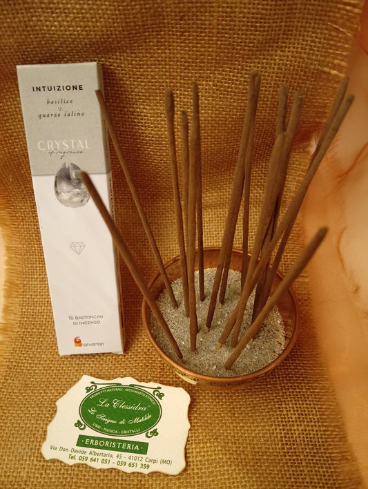 Confezione di Incenso Crystal Fragrance Intuizione Dhanvantari appoggiata accanto a una ciotola di rame con sedici bastoncini inseriti nella sabbia e al biglietto da visita dell’Erboristeria La Clessidra Carpi su sfondo in telo di yuta
