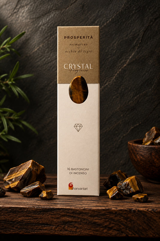 Astuccio rettangolare verticale di Incenso Crystal Fragrance Prosperità Dhanvantari su mensola di legno scuro davanti a una parete di ardesia con frammenti grezzi di pietra occhio di tigre, da Erboristeria La Clessidra Carpi.