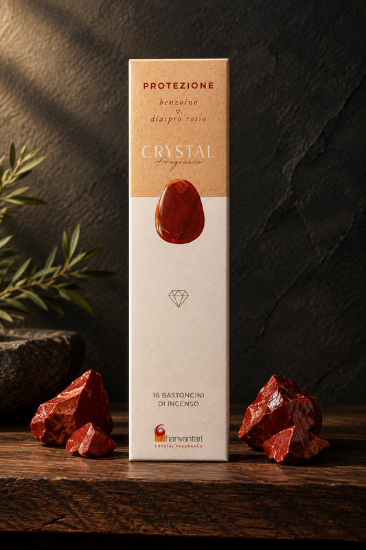 Astuccio rettangolare verticale di Incenso Crystal Fragrance Protezione Dhanvantari su mensola di legno scuro davanti a una parete di ardesia con frammenti grezzi di pietra diaspro rosso, da Erboristeria La Clessidra Carpi.