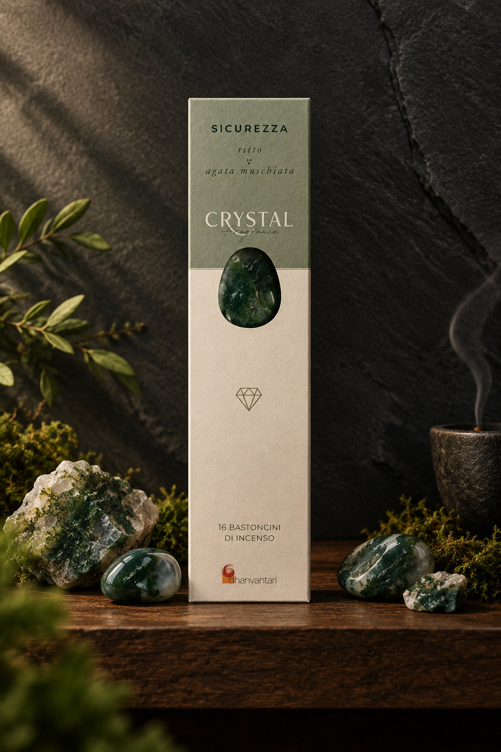 Astuccio rettangolare verticale di Incenso Crystal Fragrance Sicurezza Dhanvantari su mensola di legno scuro davanti a una parete di ardesia con frammenti grezzi di agata muschiata verde, da Erboristeria La Clessidra Carpi.