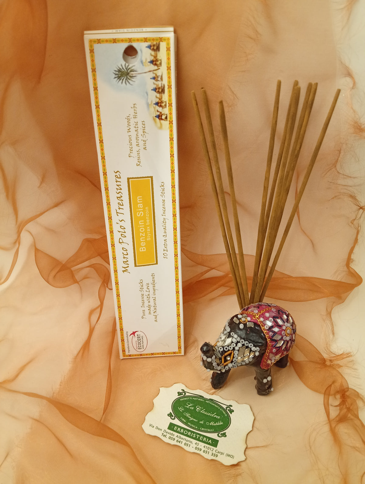 Incenso Benzoin Siam Fiore d'Oriente Linea Marco Polo's Treasures con astuccio ben visibile, mazzetto di incensi reali, biglietto da visita e velo sullo sfondo, esposto in negozio da Erboristeria La Clessidra Carpi.