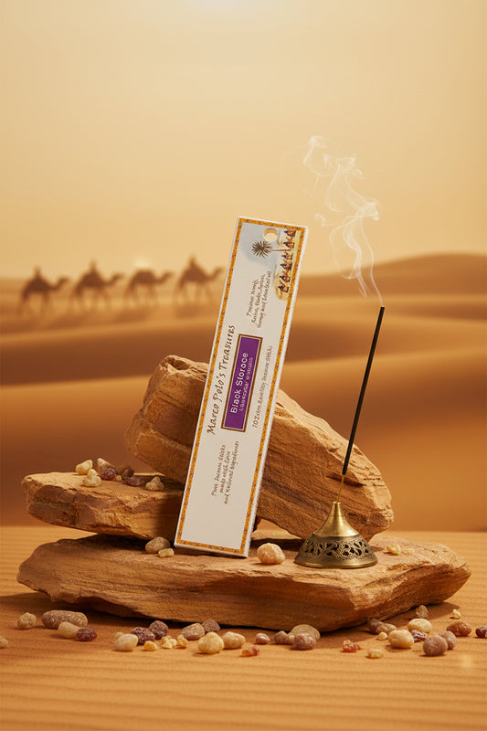 Incenso biologico Black Storace Fiore d'Oriente Linea Marco Polo's Treasures posizionato in verticale su una roccia nel deserto al tramonto con carovana sullo sfondo, acquistabile online e in negozio da Erboristeria La Clessidra Carpi.