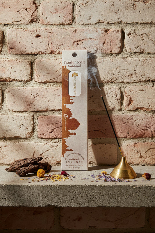 Incenso Frankincense Olibano Fiore d'Oriente Linea Traditional con stick acceso in portaincenso di ottone, cortecce e fiori su base di pietra e muro antico, da Erboristeria La Clessidra Carpi.
