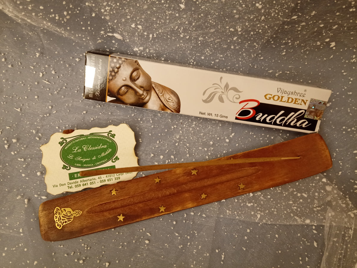Confezione orizzontale di Incenso Golden Nag Buddha (Buddha) Vijayshree appoggiata su barchetta di legno portaincenso con biglietto da visita dell’Erboristeria La Clessidra Carpi e sfondo con velo trasparente grigio azzurro puntinato di bianco