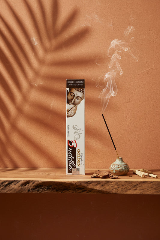 Astuccio di Incenso Golden Nag Buddha (Buddha) Vijayshree su mensola di legno grezzo davanti a parete terracotta con ombre di foglie di palma, portaincenso artigianale con stick e scaglie di corteccia, da Erboristeria La Clessidra Carpi.