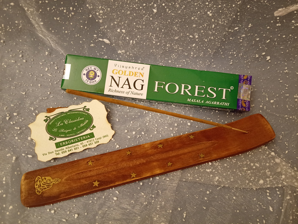 Confezione orizzontale di Incenso Golden Nag Forest Vijayshree appoggiata su barchetta di legno portaincenso con biglietto da visita dell’Erboristeria La Clessidra Carpi e sfondo con velo trasparente grigio azzurro puntinato di bianco