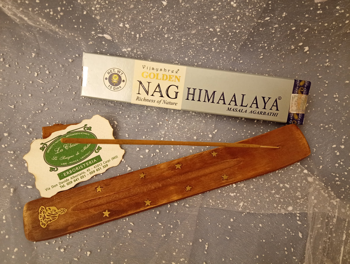 Confezione orizzontale di Incenso Golden Nag Himaalaya Vijayshree appoggiata su barchetta di legno portaincenso con biglietto da visita dell’Erboristeria La Clessidra Carpi e sfondo con velo trasparente grigio azzurro puntinato di bianco