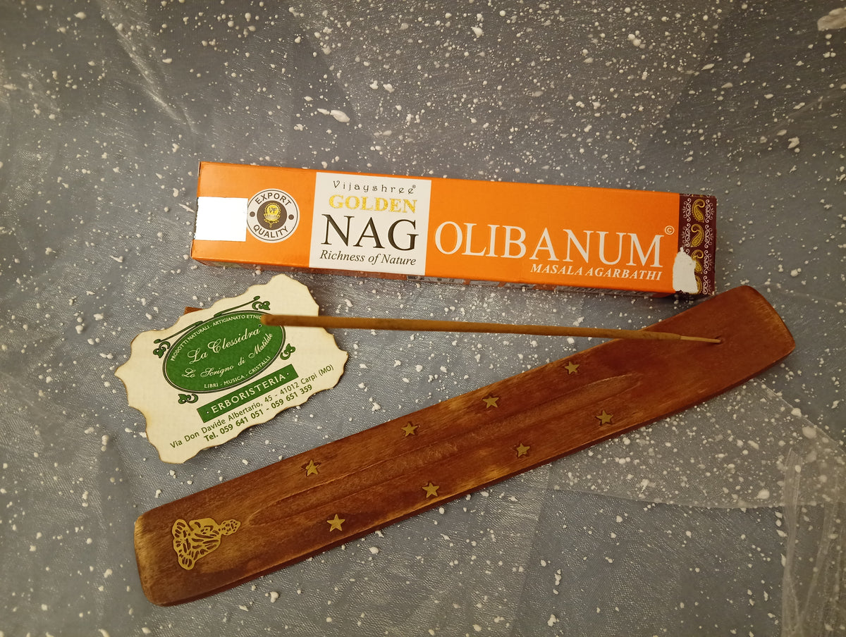 Confezione orizzontale di Incenso Golden Nag Olibanum Vijayshree appoggiata su barchetta di legno portaincenso con biglietto da visita dell’Erboristeria La Clessidra Carpi e sfondo con velo trasparente grigio azzurro puntinato di bianco