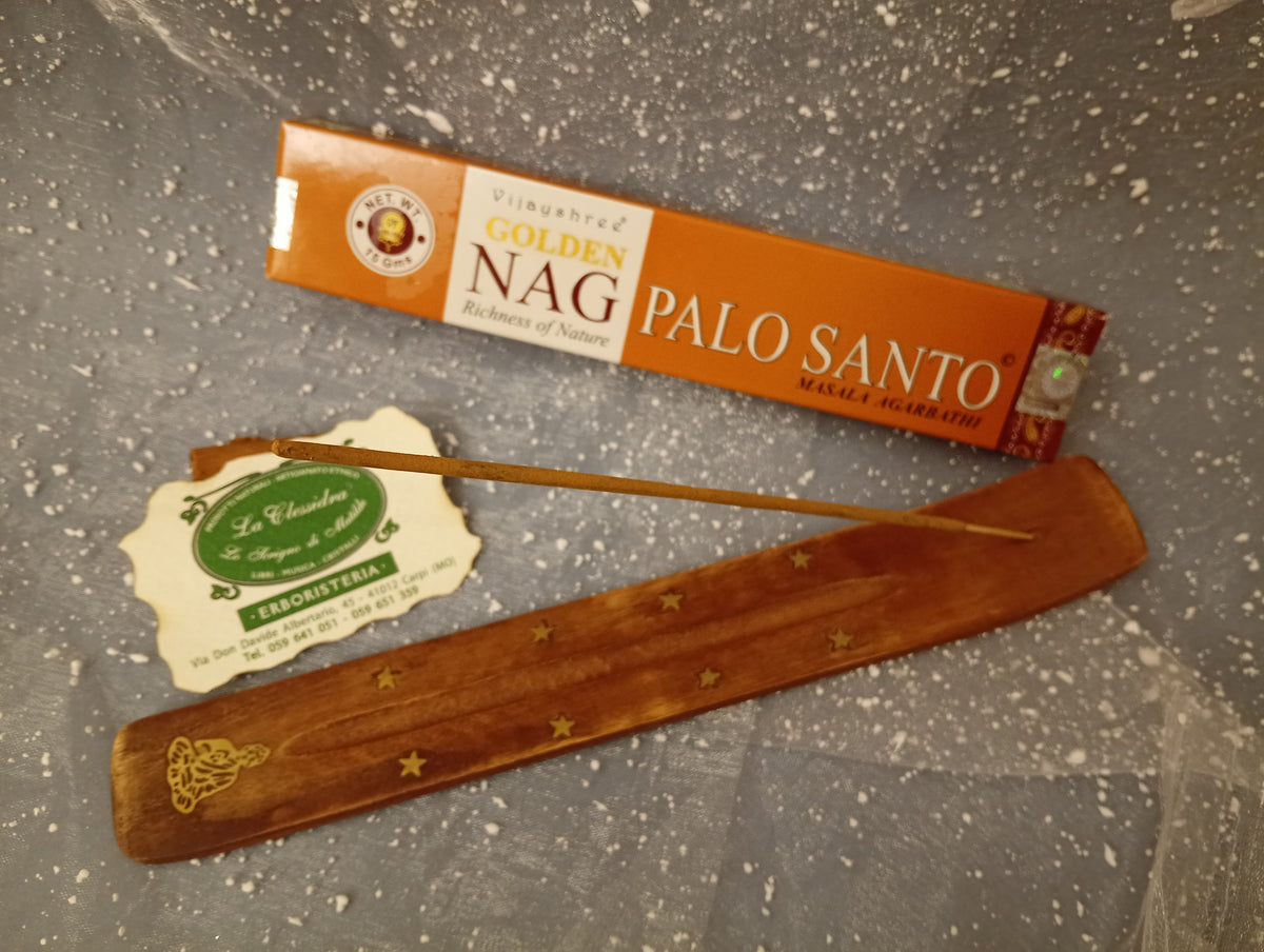 Confezione orizzontale di Incenso Golden Nag Palo Santo Vijayshree appoggiata su barchetta di legno portaincenso con biglietto da visita dell’Erboristeria La Clessidra Carpi e sfondo con velo trasparente grigio azzurro puntinato di bianco