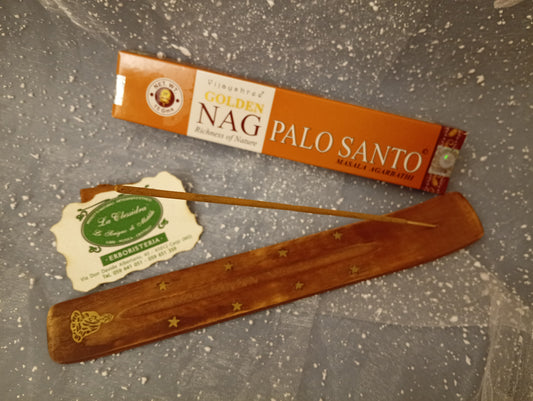 Confezione orizzontale di Incenso Golden Nag Palo Santo Vijayshree appoggiata su barchetta di legno portaincenso con biglietto da visita dell’Erboristeria La Clessidra Carpi e sfondo con velo trasparente grigio azzurro puntinato di bianco