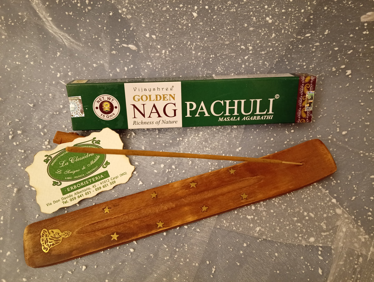 Confezione orizzontale di Incenso Golden Nag Patchouli Vijayshree appoggiata su barchetta di legno portaincenso con biglietto da visita dell’Erboristeria La Clessidra Carpi e sfondo con velo trasparente grigio azzurro puntinato di bianco.