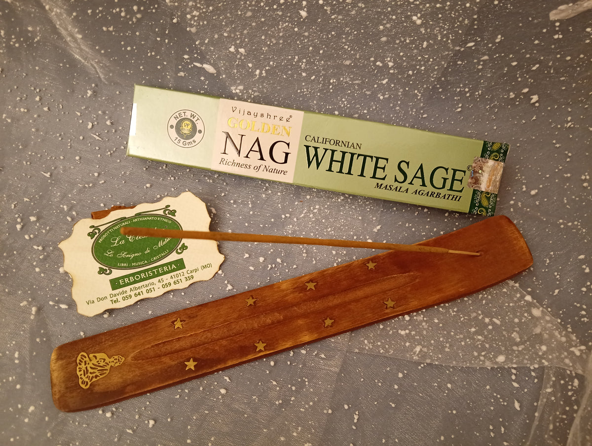 Confezione orizzontale di Incenso Golden Nag White Sage (Salvia Bianca) Vijayshree appoggiata su barchetta di legno portaincenso con biglietto da visita dell’Erboristeria La Clessidra Carpi e sfondo con velo trasparente grigio azzurro puntinato di bianco