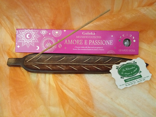 Confezione orizzontale di Incenso Goloka Manifestation Amore e Passione con Quarzo Rosa burattato, davanti a un portaincenso artigianale a forma di foglia con stick, biglietto da visita dell’Erboristeria La Clessidra Carpi e sfondo con telo sfumato in toni aranciati orientali.