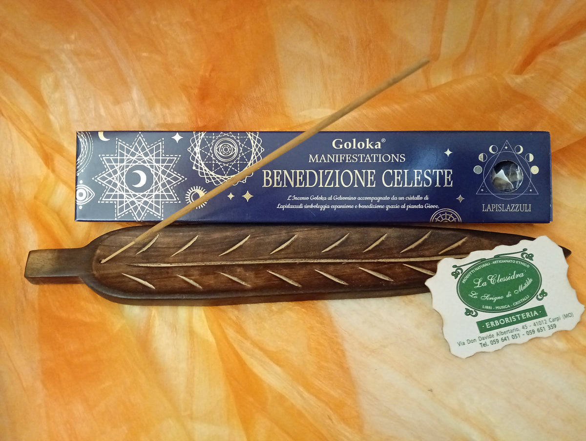 Confezione orizzontale di Incenso Goloka Manifestation Benedizione Celeste con Lapislazzuli burattato, davanti a un portaincenso artigianale a forma di foglia con stick, biglietto da visita dell’Erboristeria La Clessidra Carpi e sfondo con telo sfumato in toni aranciati orientali.