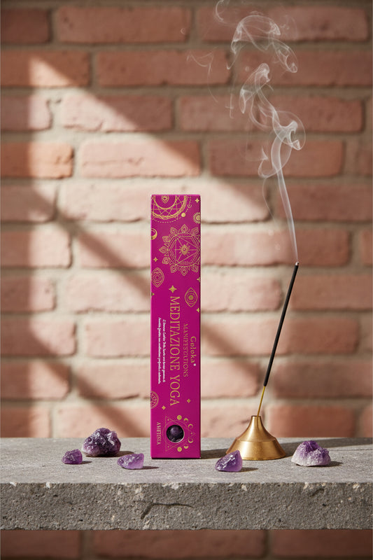 Astuccio Incenso Goloka Manifestation Meditazione Yoga su mensola di pietra con frammenti di Ametista, portaincenso metallico con stick acceso e muro antico, da Erboristeria La Clessidra Carpi.
