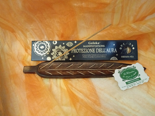Confezione orizzontale di Incenso Goloka Manifestation Protezione dell'Aura con Ossidiana Nera burattata, davanti a un portaincenso artigianale a forma di foglia con stick, biglietto da visita dell’Erboristeria La Clessidra Carpi e sfondo con telo sfumato in toni aranciati orientali.