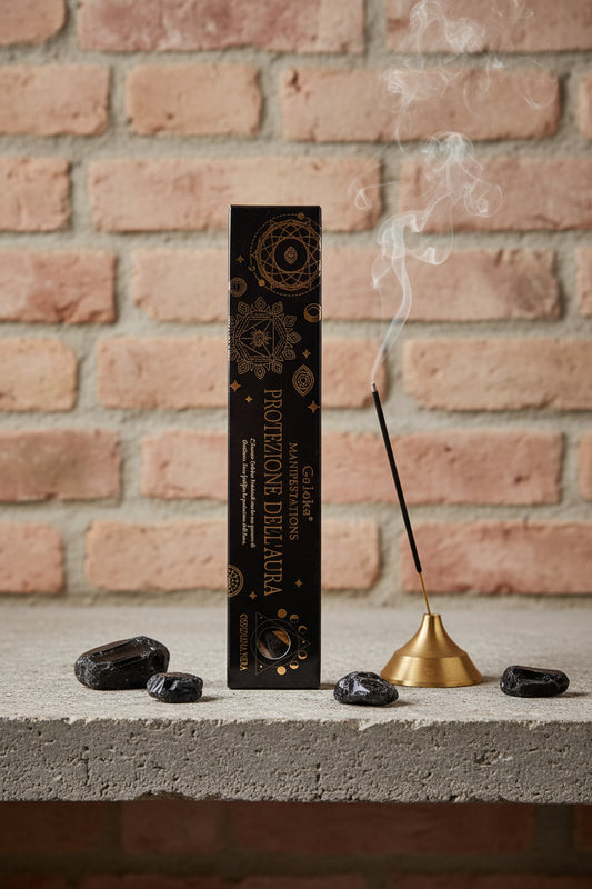 Astuccio Incenso Goloka Manifestation Protezione dell'Aura su mensola di pietra con frammenti di Ossidiana Nera, portaincenso metallico con stick acceso e muro antico, da Erboristeria La Clessidra Carpi.