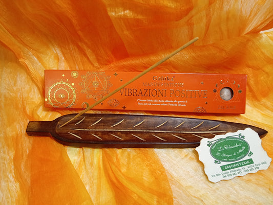 Confezione orizzontale di Incenso Goloka Manifestation Vibrazioni Positive con Pietra del Sole burattata, davanti a un portaincenso artigianale a forma di foglia con stick, biglietto da visita dell’Erboristeria La Clessidra Carpi e sfondo con telo sfumato in toni aranciati orientali.
