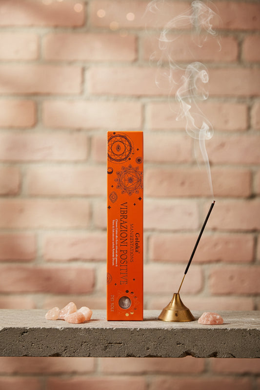 Astuccio Incenso Goloka Manifestation Vibrazioni Positive su mensola di pietra con frammenti di Pietra del Sole, portaincenso metallico con stick acceso e muro antico, da Erboristeria La Clessidra Carpi.