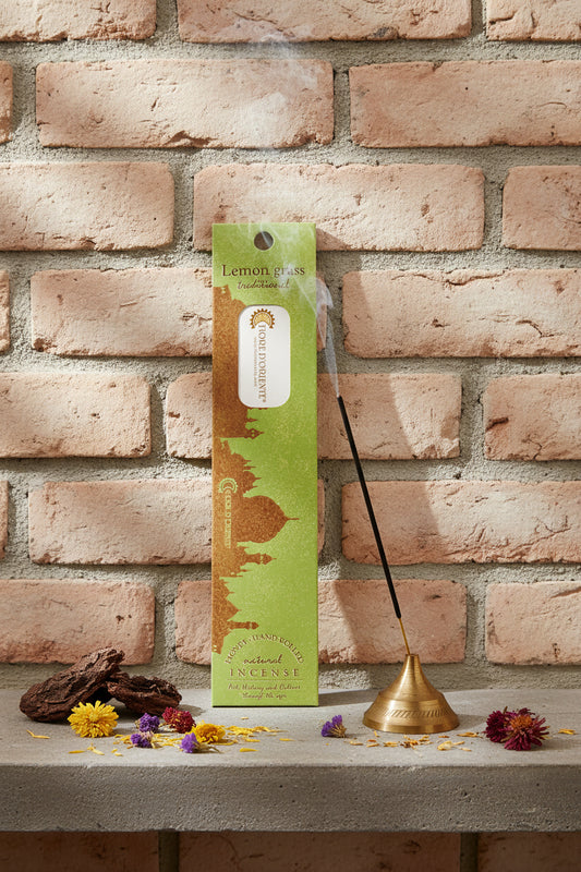 Incenso Lemongrass Citronella Fiore d'Oriente Linea Traditional con stick acceso in portaincenso di ottone, cortecce e fiori su base di pietra e muro antico, da Erboristeria La Clessidra Carpi.