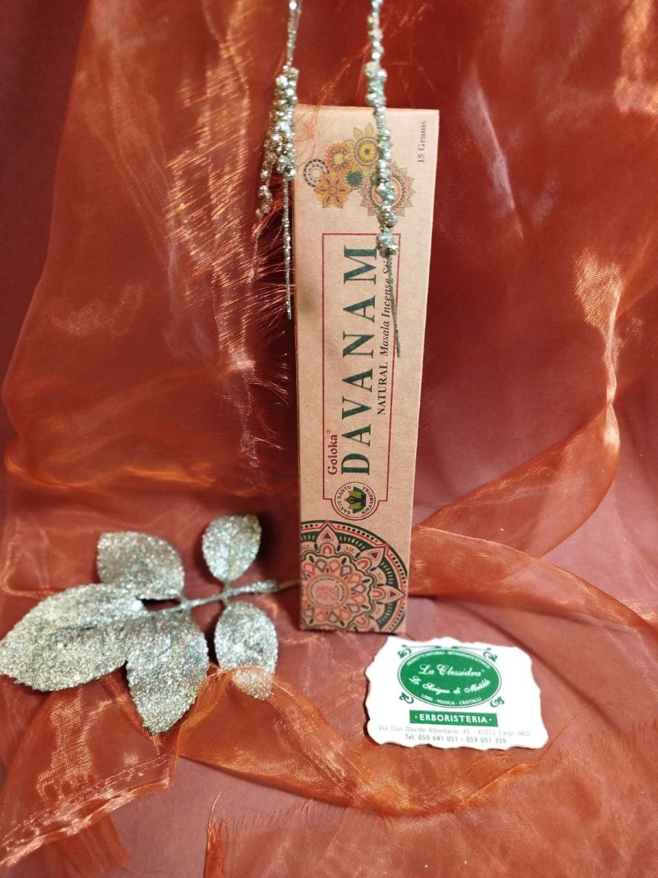 Incenso Goloka Natural Davanam su tessuto arancione con decorazioni argentate e biglietto del negozio La Clessidra a Carpi