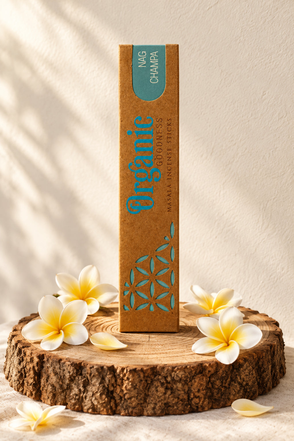 Confezione in cartone kraft di Incenso Organic Goodness Nag Champa Song of India in verticale su sezione di tronco di legno con fiori di plumeria champa, da Erboristeria La Clessidra Carpi