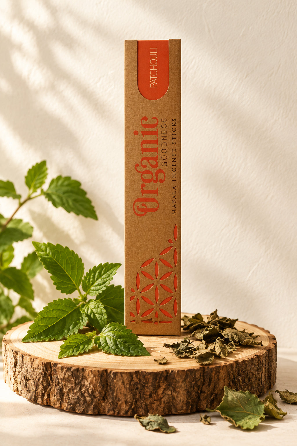 Confezione in cartone kraft di Incenso Organic Goodness Patchouli Song of India in verticale su sezione di tronco di legno con foglie aromatiche di patchouli, da Erboristeria La Clessidra Carpi