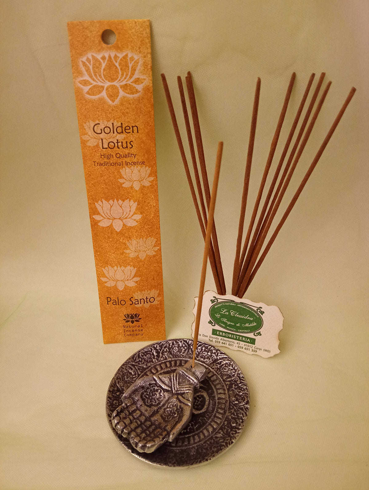 Incenso Palo Santo Fiore d'Oriente Linea Golden Lotus, astuccio con mazzetto di bastoncini aperti in piedi, portaincenso in metallo con mano e biglietto da visita esposti da Erboristeria La Clessidra Carpi.