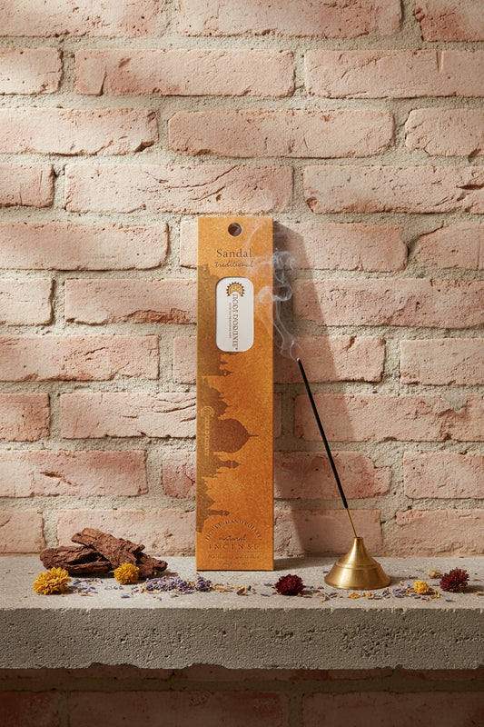Incenso Sandal Sandalo Fiore d'Oriente Linea Traditional con stick acceso in portaincenso di ottone, cortecce e fiori su base di pietra e muro antico, da Erboristeria La Clessidra Carpi.