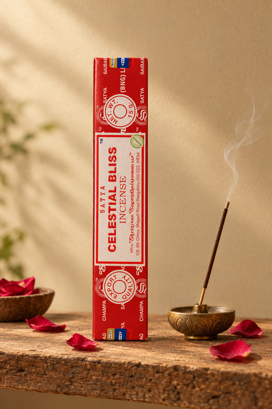 Astuccio rettangolare verticale di Incenso Celestial Bliss Satya su mensola di legno grezzo davanti a una parete di intonaco beige sabbia con una luce soffusa e sfumata sul retro e petali di rosa sparsi, da Erboristeria La Clessidra Carpi