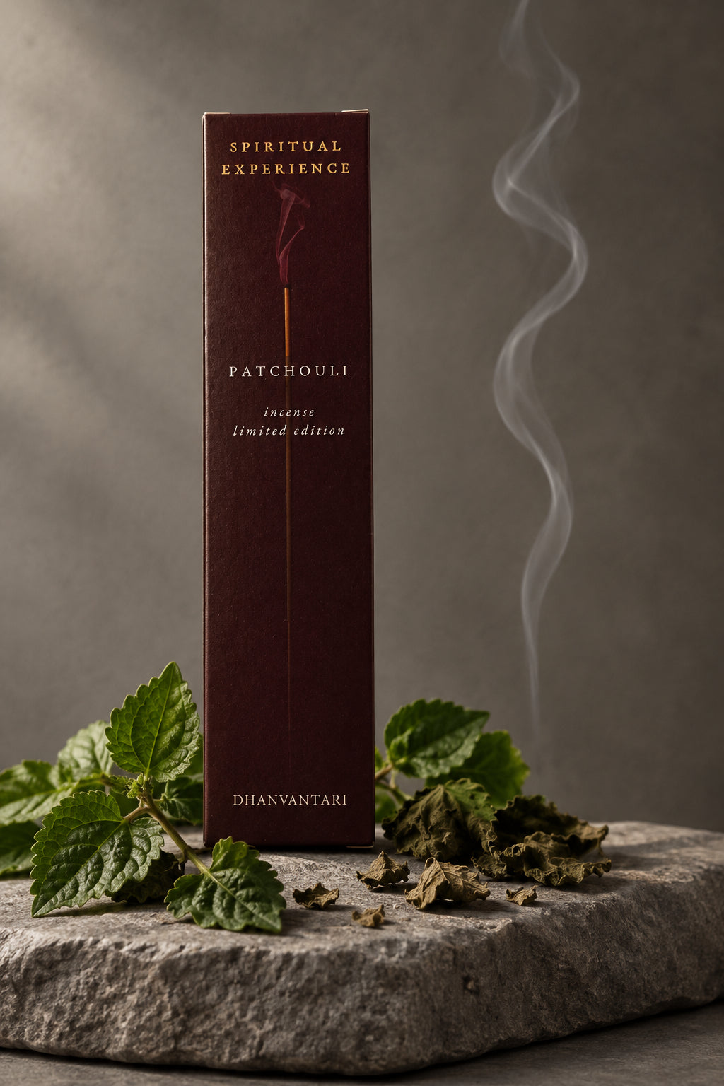 Astuccio rettangolare di Incenso Spiritual Experience Patchouli Dhanvantari in verticale su lastra di pietra grigia davanti a parete scura con foglie di patchouli, da Erboristeria La Clessidra Carpi