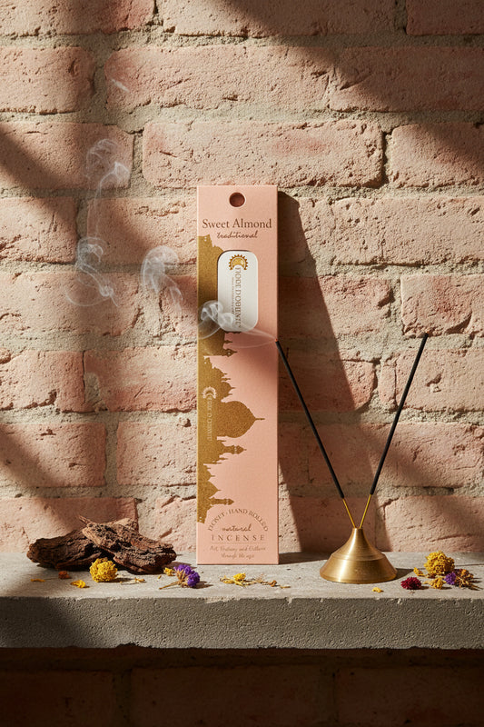 Incenso Sweet Almond Mandorla Fiore d'Oriente Linea Traditional con stick acceso in portaincenso di ottone, cortecce e fiori su base di pietra e muro antico, da Erboristeria La Clessidra Carpi