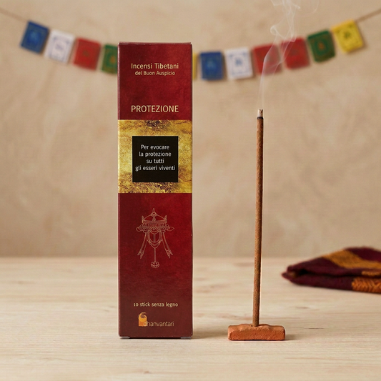 Incenso Tibetano del Buon Auspicio Dhanvantari Protezione su legno chiaro, con bastoncino acceso in portaincenso di terracotta e bandierine tibetane sfocate sullo sfondo