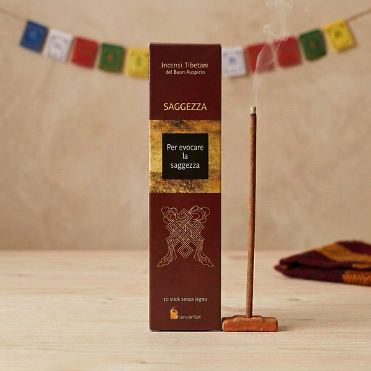 Incenso Tibetano del Buon Auspicio Dhanvantari Saggezza su legno chiaro, con bastoncino acceso e bandierine tibetane sfocate