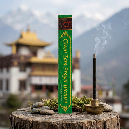 Confezione di incenso tibetano Green Tara Prayer Himalayan Arts su un tronco con sassi e muschio, accanto a un bastoncino acceso, con tempio tibetano e montagne sullo sfondo