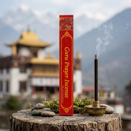 Confezione di incenso tibetano Guru Prayer Himalayan Arts su un tronco con sassi e muschio, accanto a un bastoncino acceso, con tempio tibetano e montagne sullo sfondo