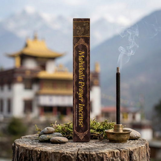 Confezione di incenso tibetano Mahakala Prayer Himalayan Arts su un tronco con sassi e muschio, accanto a un bastoncino acceso, con tempio tibetano e montagne sullo sfondo