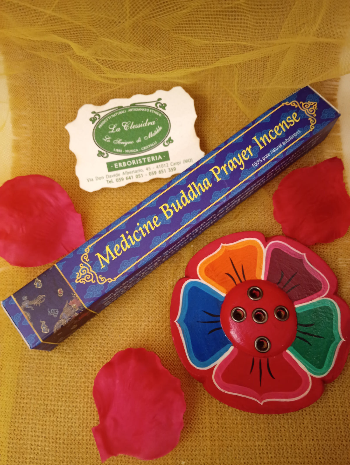 Confezione di incenso tibetano Medicine Buddha Prayer Himalayan Arts con portaincenso a fiore colorato, petali di rosa e biglietto di Erboristeria La Clessidra Carpi su tessuto dorato.